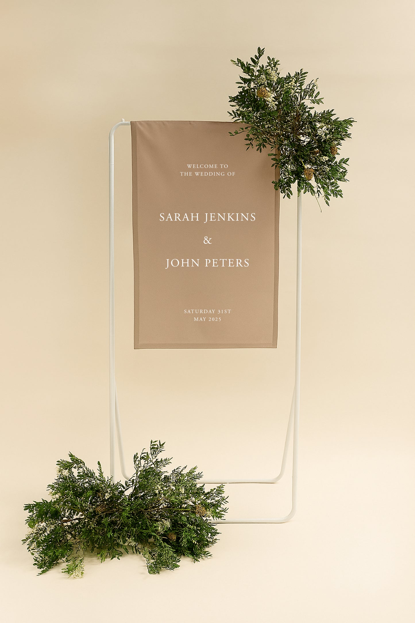 Wedding welcome sign with names and date, framed by greenery on a beige background