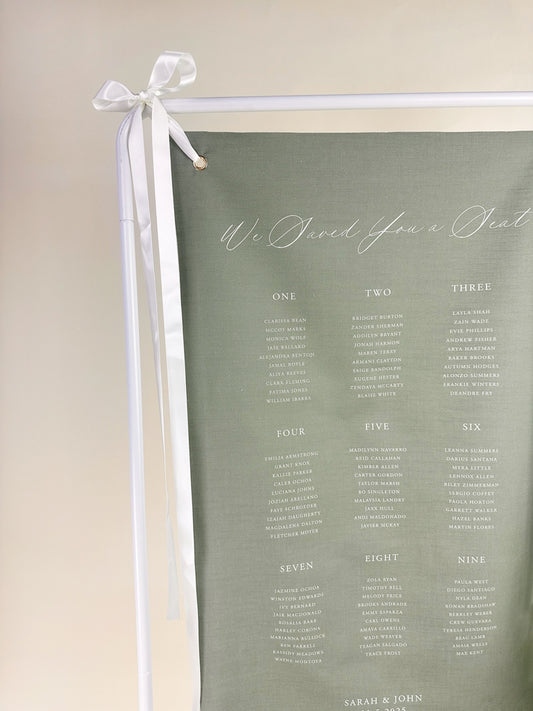 Sage green seating chart with a white ribbon on a beige background