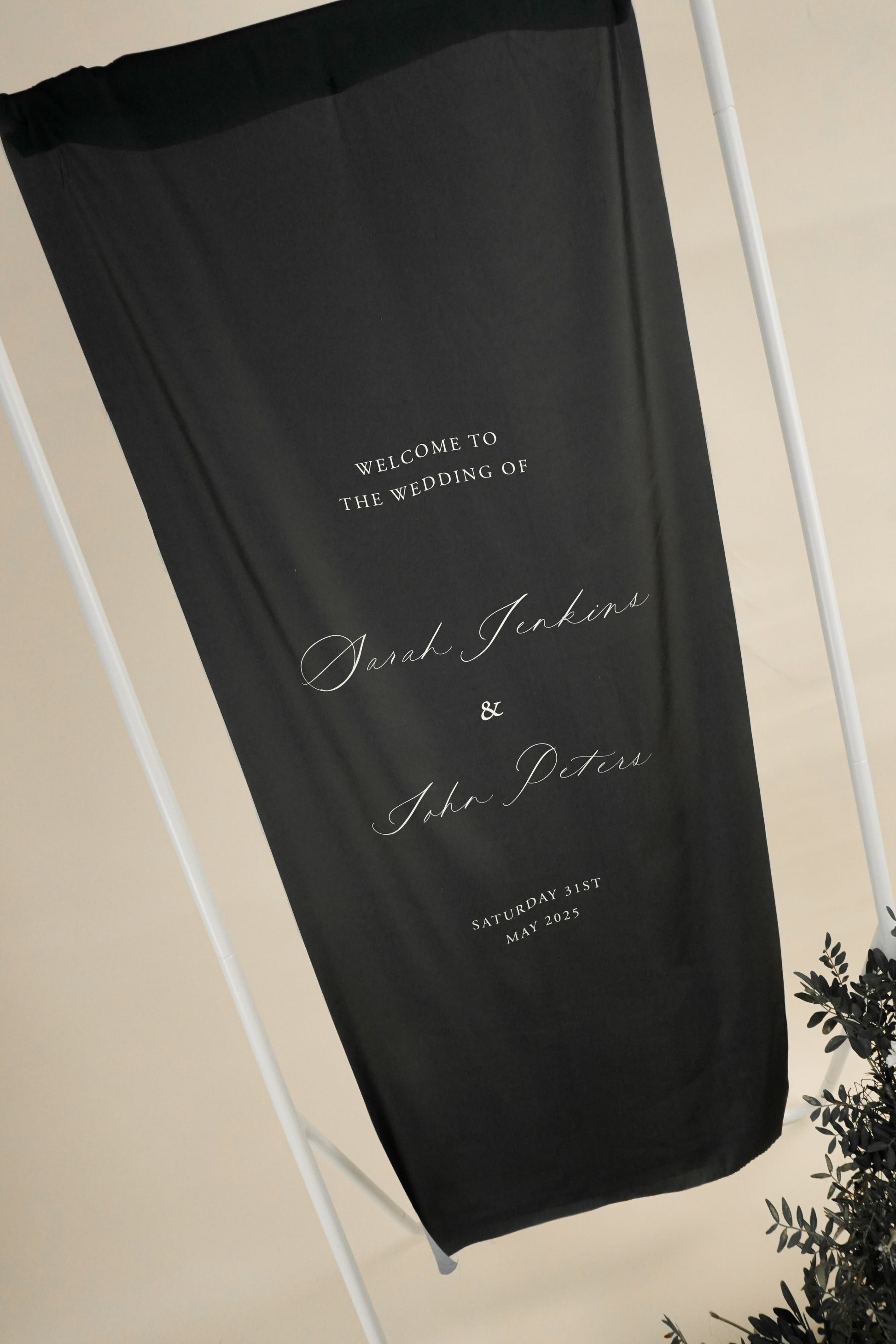 Black wedding welcome sign with white text on a stand against a beige background