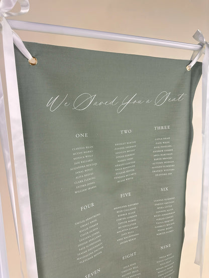 Green fabric with white text and 'We Saved You a Seat' printed on it, hanging from a stand.