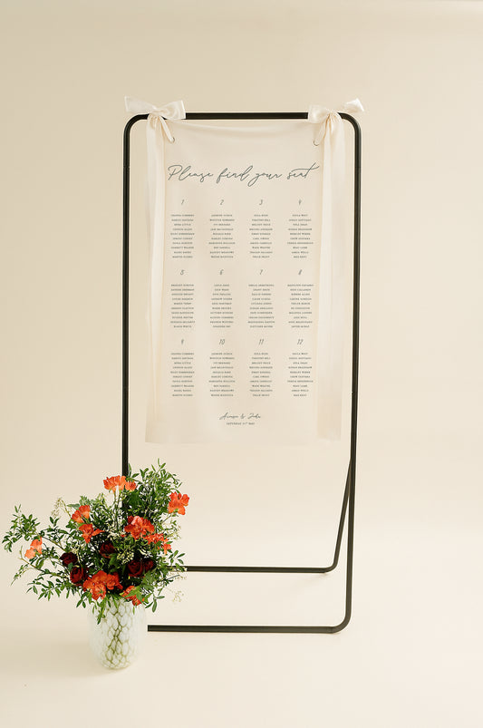 Seating chart on a stand with flowers in a vase on a beige background